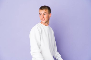 Genç beyaz yakışıklı adam gülümseyen, neşeli ve keyifli bir şekilde yana bakıyor..