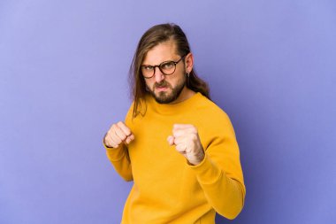 Uzun saçlı genç adam kameraya yumruğunu gösteriyor, agresif yüz ifadesi..