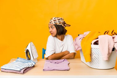 Elbiseleri ütüleyen genç İspanyol kadın. Gülümsüyor, neşeli ve keyifli görünüyor..