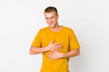 Genç beyaz yakışıklı adam mutlu bir şekilde gülüyor ve ellerini karnının üstünde tutarak eğleniyor..