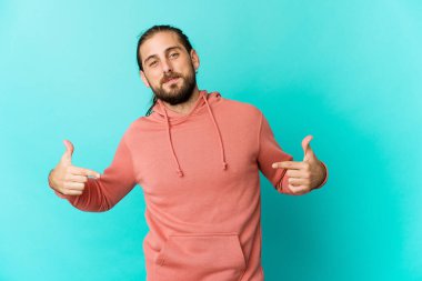 Uzun saçlı genç bir adam gömleğin fotokopi odasını elle işaret ediyor, gururlu ve kendinden emin.