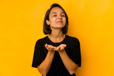 Genç İspanyol kadın sarıda izole edilmiş. Elinde avuç içi olan bir şeyle kameraya sunuyor..