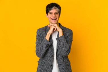 Young skinny hispanic man keeps hands under chin, is looking happily aside.