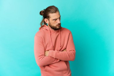 Uzun saçlı, hoşnutsuzca kaşlarını çatmış, kollarını kavuşturmuş genç bir adam..