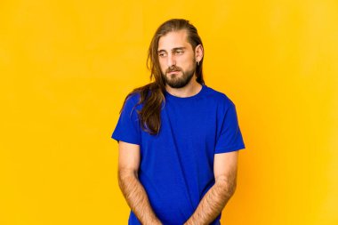 Uzun saçlı genç adam üzgün, ciddi yüzlü, mutsuz ve hoşnutsuz görünüyor..