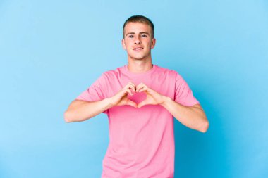 Beyaz tenli yakışıklı adam gülümsüyor ve elleriyle kalp şeklini gösteriyor..