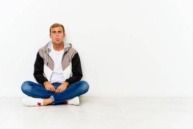 Genç, beyaz bir adam yerde oturuyor. Komik ve dostane bir dille..