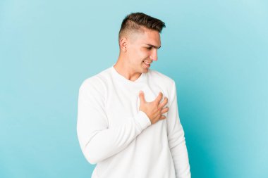 Genç, beyaz tenli yakışıklı bir adam yalnız başına gülüyor, elini kalbine koyuyor, mutluluk kavramını koruyor..