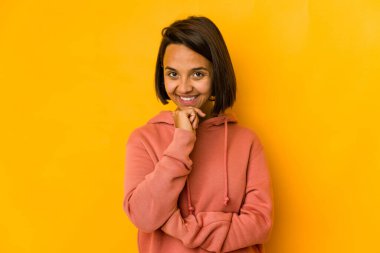 Genç İspanyol kadın sarıda izole edilmiş mutlu ve kendinden emin gülümseyen, elleriyle çenesine dokunan.