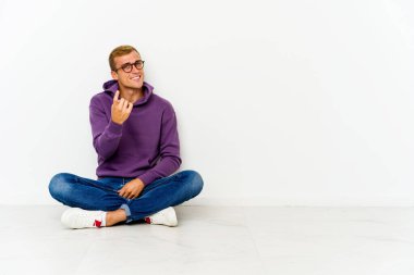 Genç, beyaz bir adam yerde oturuyor ve seni işaret ediyor. Sanki seni davet ediyormuş gibi..