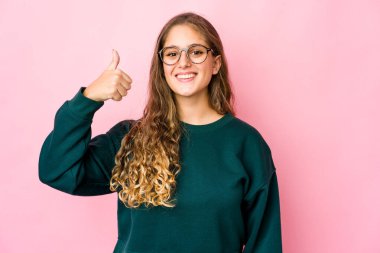 Genç beyaz kadın gülümsüyor ve başparmağını kaldırıyor.