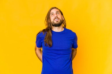 Uzun saçlı genç adam rahat görünüyor ve mutlu gülüyor, boynunu uzatmış dişlerini gösteriyor..