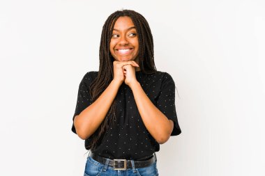 Beyaz arka planda izole edilmiş genç Afrikalı Amerikalı kadın ellerini çenesinin altında tutuyor ve mutlu bir şekilde yan tarafa bakıyor..