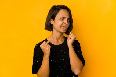 Sarıda izole edilmiş genç İspanyol kadın kameraya yumruğunu gösteriyor, agresif yüz ifadesi..