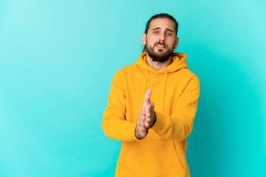 Uzun saçlı genç adam enerjik ve rahat görünüyor, ellerini ovuşturarak kendinden emin..