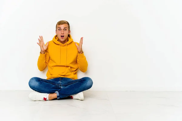 stock image Young caucasian man sitting on the floor celebrating a victory or success, he is surprised and shocked.