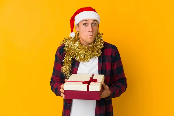 Junger Kaukasischer Mann Mit Weihnachtsmütze Und Geschenk Auf Gelbem Hintergrund — Stockfoto