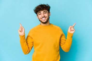 Mavi arka plandaki genç Arap adam farklı kopya alanlarını gösteriyor, birini seçiyor, parmaklarıyla gösteriyor.