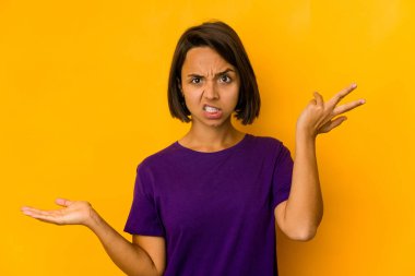 Genç İspanyol kadın, sarı renkte izole edilmiş, kafası karışmış ve omuz silkiyor. Kopya alanını tutmak için..