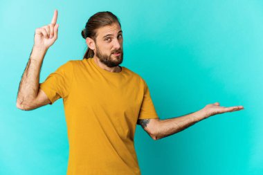 Uzun saçlı genç adam elinde bir ürünü tutuyor ve gösteriyor..