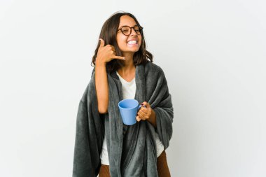 Beyaz arka planda battaniyeli genç Latin kadın parmaklarıyla bir cep telefonu hareketi gösteriyor..