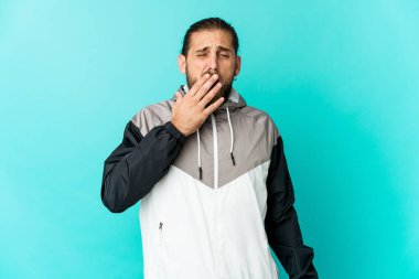 Uzun saçlı genç adam esnemiş görünüyor. Ağzı eliyle kapatan yorgun bir jest yapıyor..