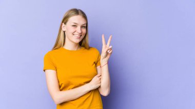 Mor arka planda izole edilmiş genç sarışın kadın iki numarayı parmaklarıyla gösteriyor..