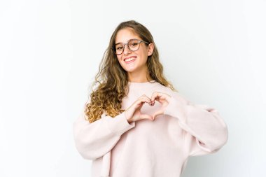 Genç beyaz kadın gülümsüyor ve elleriyle kalp şeklini gösteriyor..