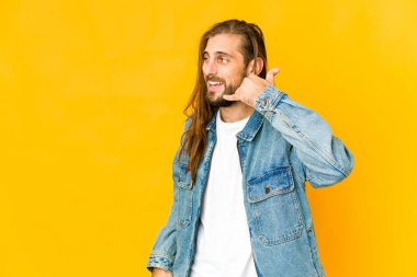 Uzun saçlı genç adam cep telefonu hareketini parmaklarıyla gösteriyor..