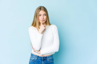 Mavi arka planda izole edilmiş genç sarışın kadın şüpheli ve şüpheci bir ifadeyle yana bakıyor..