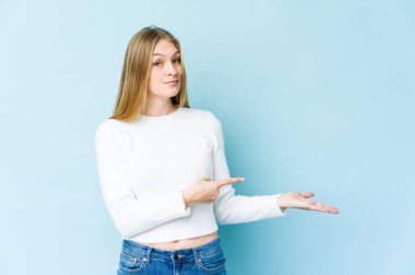 Mavi arka planda izole edilmiş genç sarışın kadın avucunun içinde bir kopyasını tutuyor..