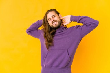 Uzun saçlı genç adam kollarını esnetiyor, rahat duruyor..