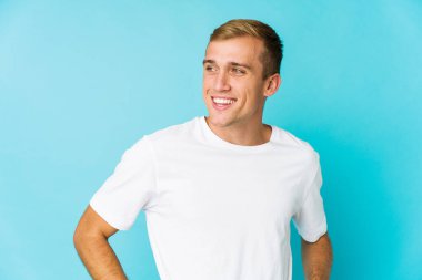 Genç beyaz yakışıklı adam mutlu bir şekilde gülüyor ve ellerini karnının üstünde tutarak eğleniyor..