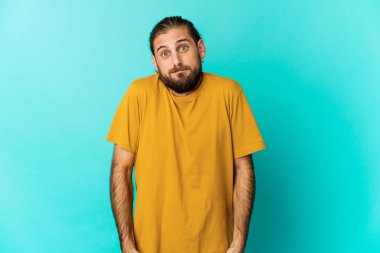 Uzun saçlı genç adam omuz silkiyor ve gözleri açık..