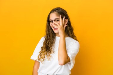 Genç beyaz kadın kameraya parmaklarıyla göz kırpıyor, utanarak yüzünü kapatıyor..