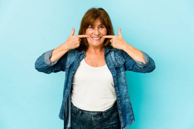 Üst düzey beyaz kadın yalnız gülüyor, parmaklarını ağzına doğrultuyor..