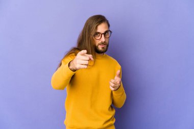 Uzun saçlı genç adam parmaklarıyla öne bakıyor..