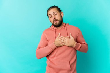 Uzun saçlı genç adam samimi bir ifadeye sahip, avuçlarını göğsüne bastırıyor. Aşk konsepti.