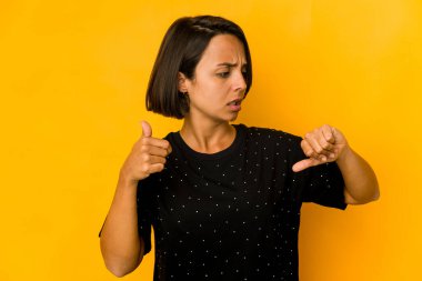 Sarıda izole edilmiş genç İspanyol kadın baş parmağını kaldırıyor ve baş parmak gösteriyor. Zor seçim konsepti.