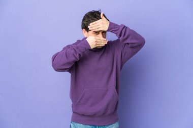 Genç havalı adam kameraya parmaklarıyla göz kırpıyor, utanarak yüzünü kapatıyor..