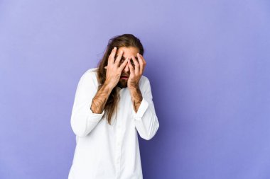 Uzun saçlı genç adam parmaklarının arasından gözünü kırp korkmuş ve gergin..