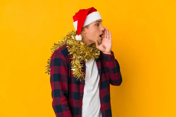 若いですCaucasian男とともにクリスマス帽子保持プレゼント隔離上の黄色の背景叫びと保持掌近くオープン口 — ストック写真