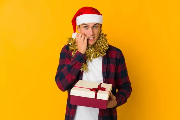 若いですCaucasian男とともにクリスマス帽子保持していますプレゼント隔離上の黄色の背景混乱 疑問と不確定な感じ — ストック写真