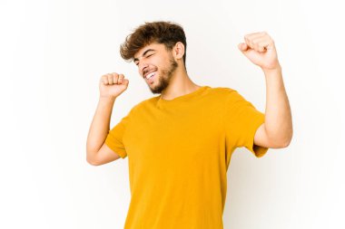 Beyaz arka planda genç bir Arap özel bir günü kutluyor, atlıyor ve enerjiyle kollarını kaldırıyor..