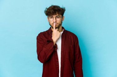 Mavi arka plandaki genç Arap adam düşünüyor ve bakıyor, yansıtıyor, düşünüyor, hayal kuruyor..