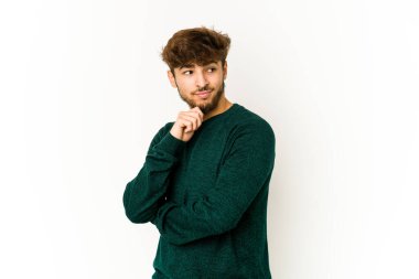 Beyaz arka planda genç bir Arap şüpheli ve şüpheci bir ifadeyle yana bakıyor..