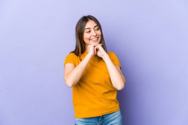 Genç beyaz kadın ellerini çenesinin altında tutuyor, mutlu bir şekilde yan tarafa bakıyor..