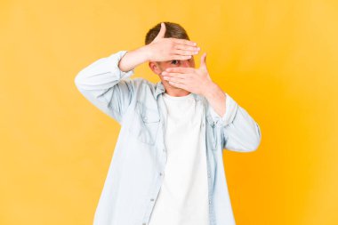 Genç, beyaz, yakışıklı bir adam kameraya parmaklarıyla göz kırpıyor, utanarak yüzünü kapatıyor..