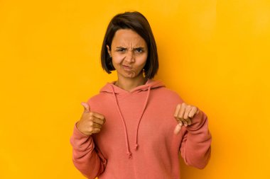 Sarıda izole edilmiş genç İspanyol kadın baş parmağını kaldırıyor ve baş parmak gösteriyor. Zor seçim konsepti.