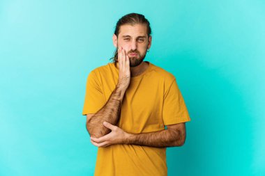 Uzun saçlı genç adam yanakları şişiriyor, yorgun bir ifade takınıyor. Yüz ifadesi kavramı.